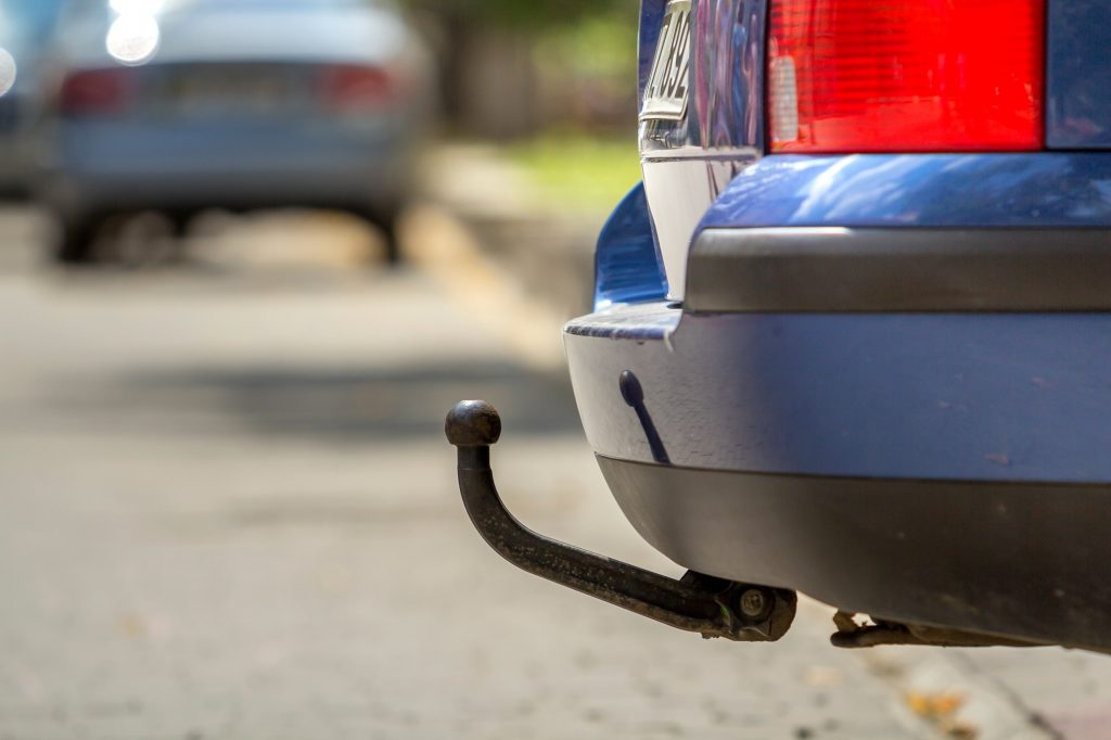 Blue car parked on sunny street, red stop lights, hook for dragging trailer, tow hitch or towbar